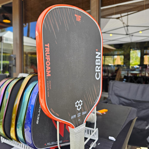 Close-up of a CRBN Trufoam Barrage pickleball paddle with orange metallic edge tape