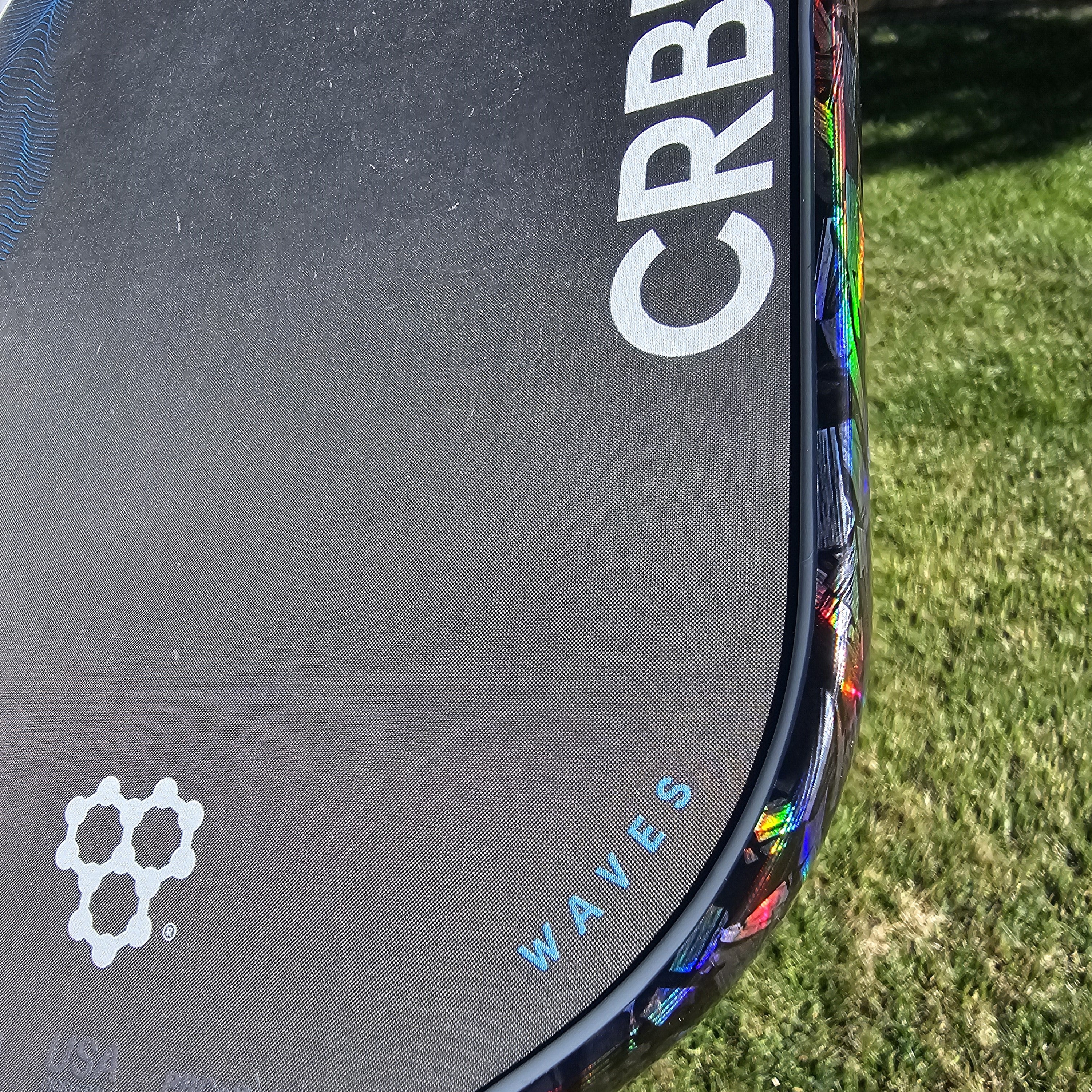 Close-up of a CRBN Waves pickleball paddle with hologram forged carbon edge tape