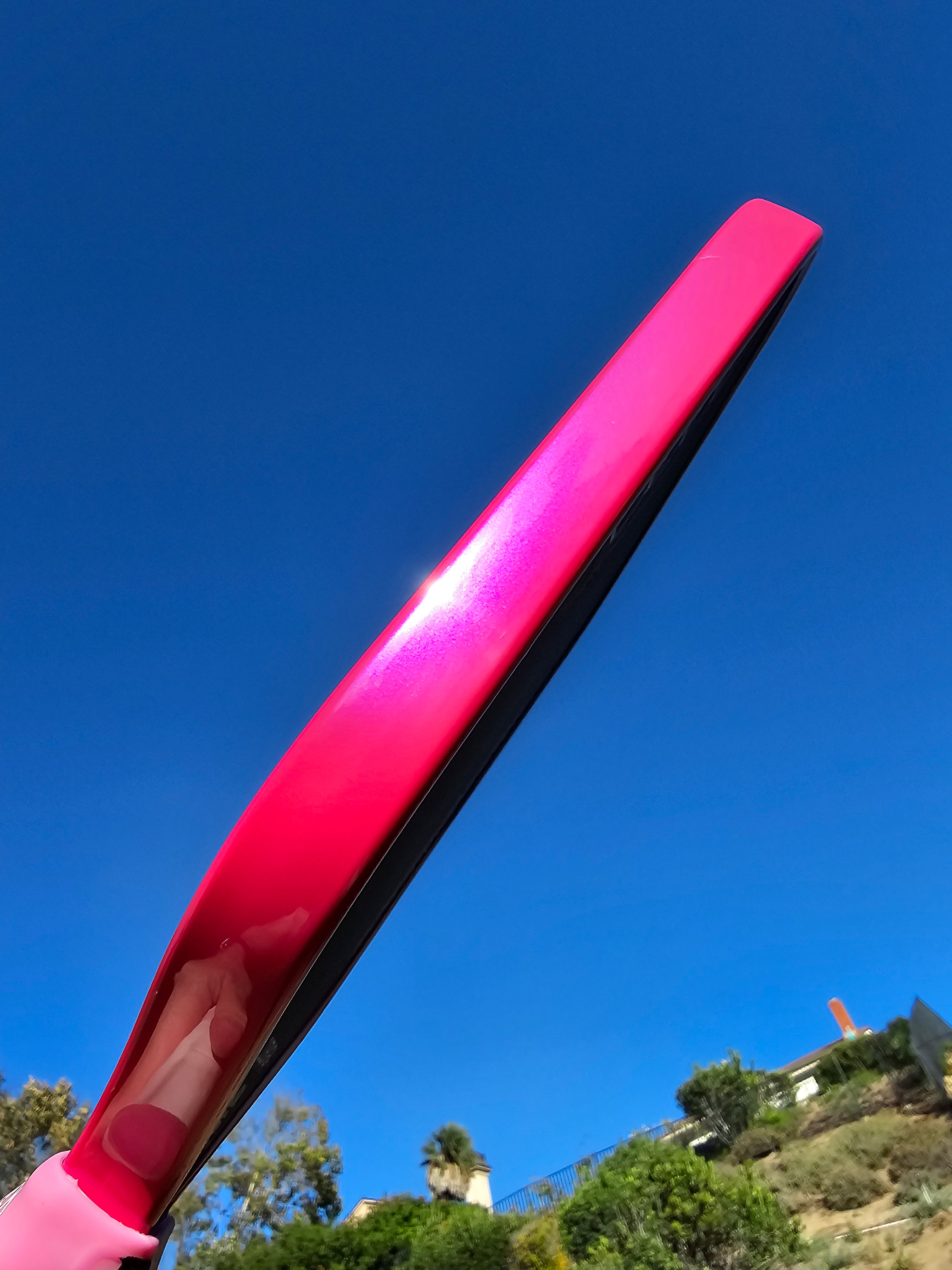 Pickleball paddle with Hot Pink/Magenta edge tape against a sky background