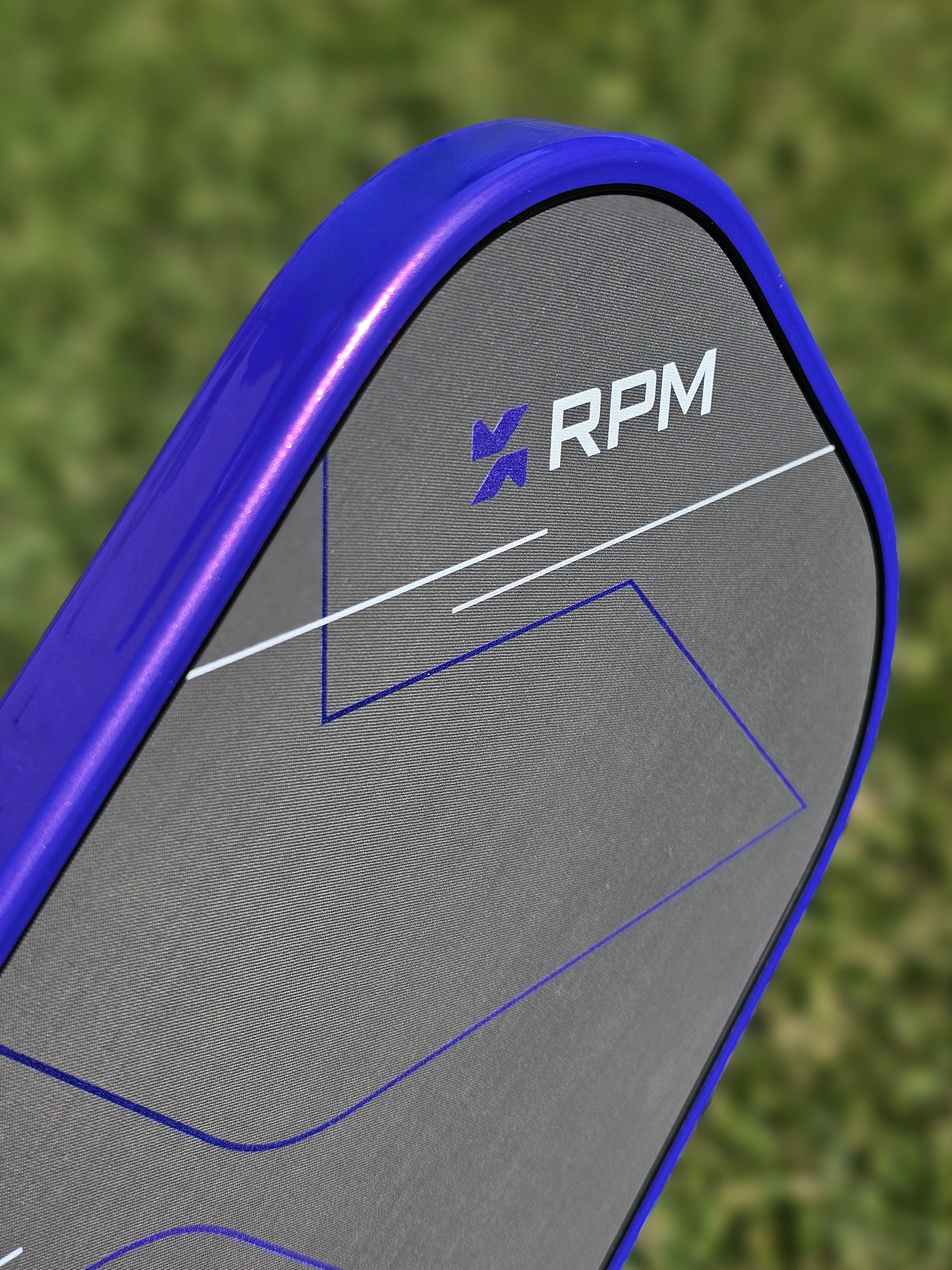 Close-up of a RPM Q2 pickleball paddle with purple ultimate edge tape