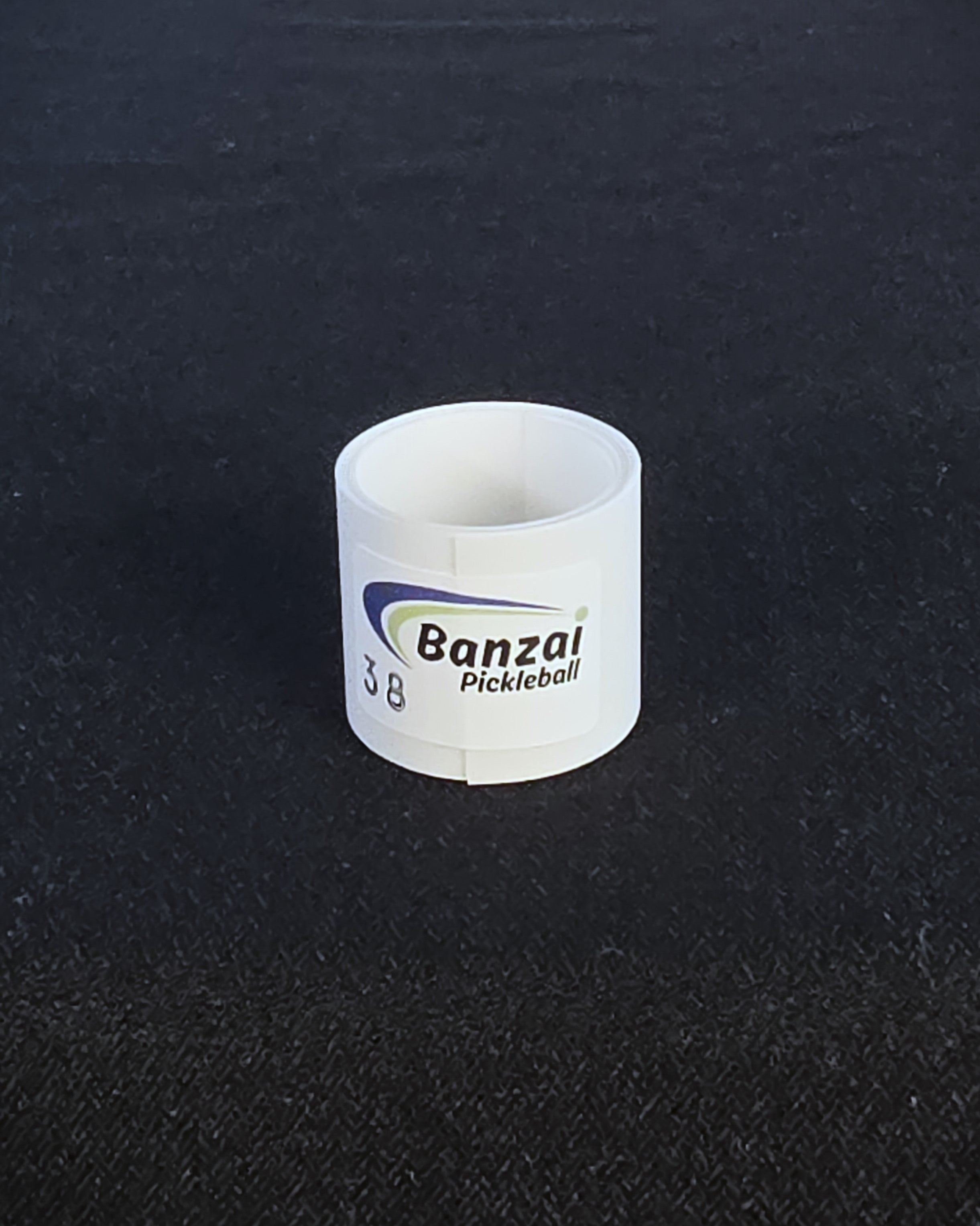 A clear roll of Banzai Pickleball edge tape shown on a black textured background.
