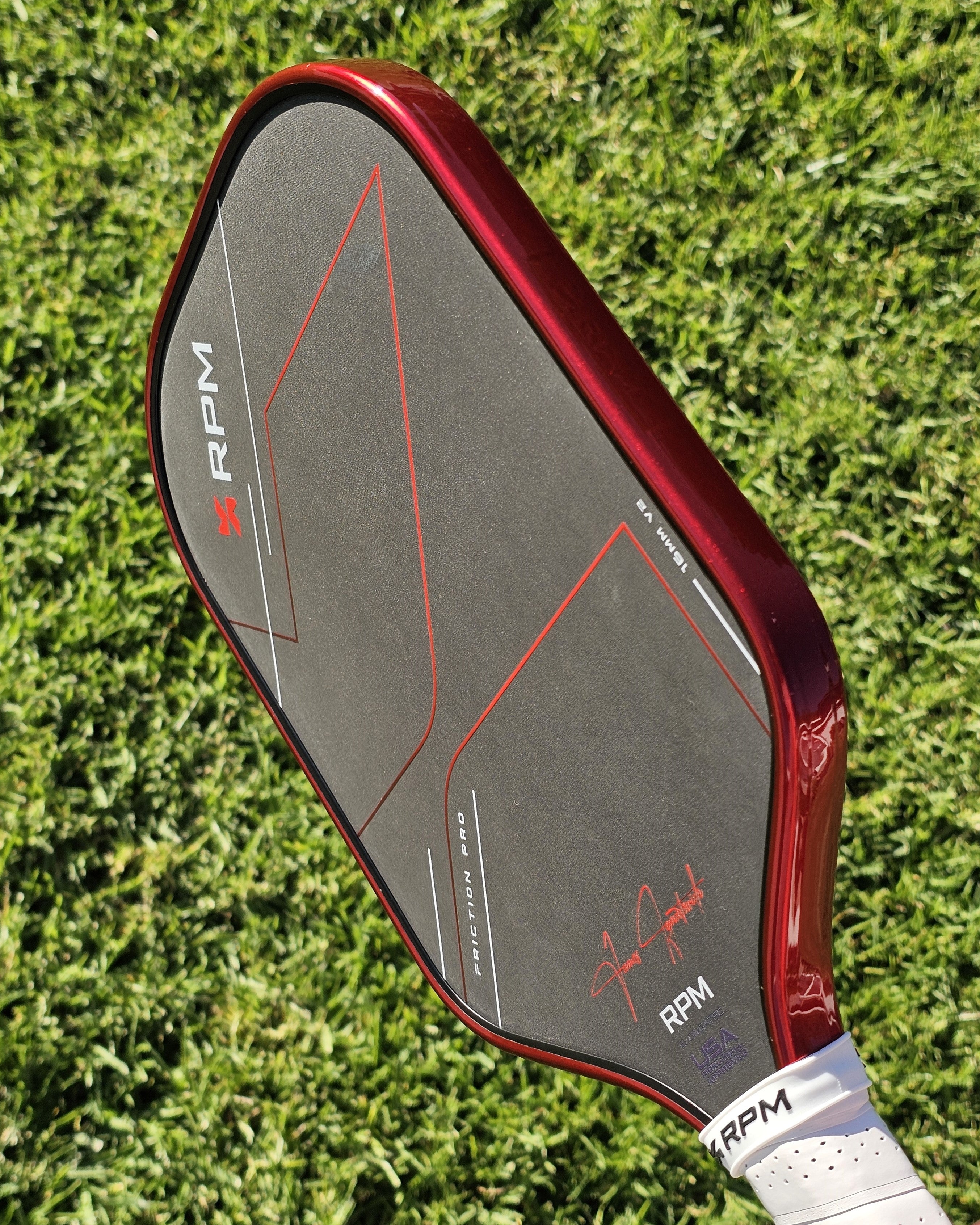 RPM Friction Pro pickleball paddle with #48 Red Candy Metallic edge tape installed shown against a grass background
