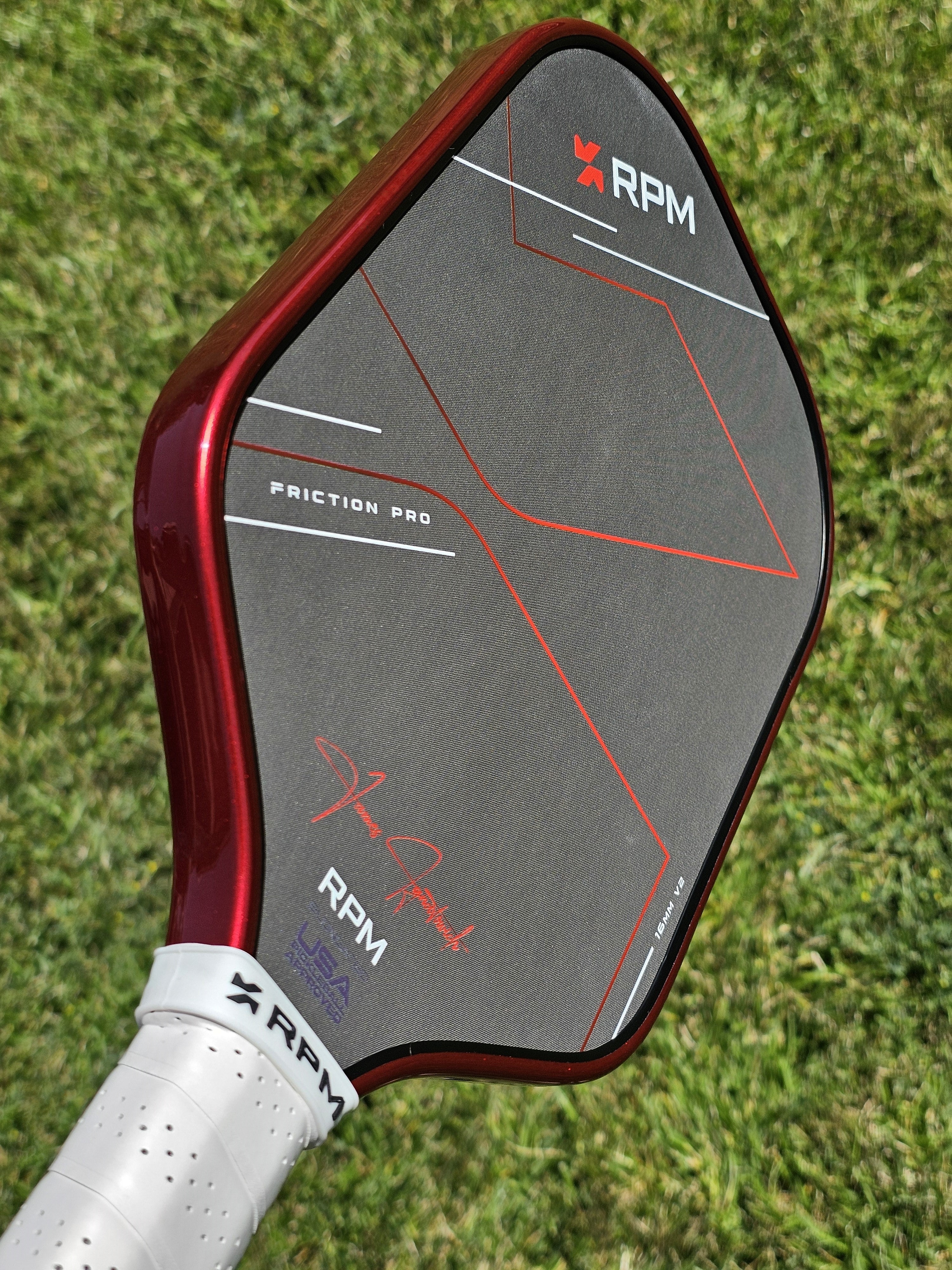 RPM Pickleball paddle with #48 Red Candy edge tape installed shown against a lawn background