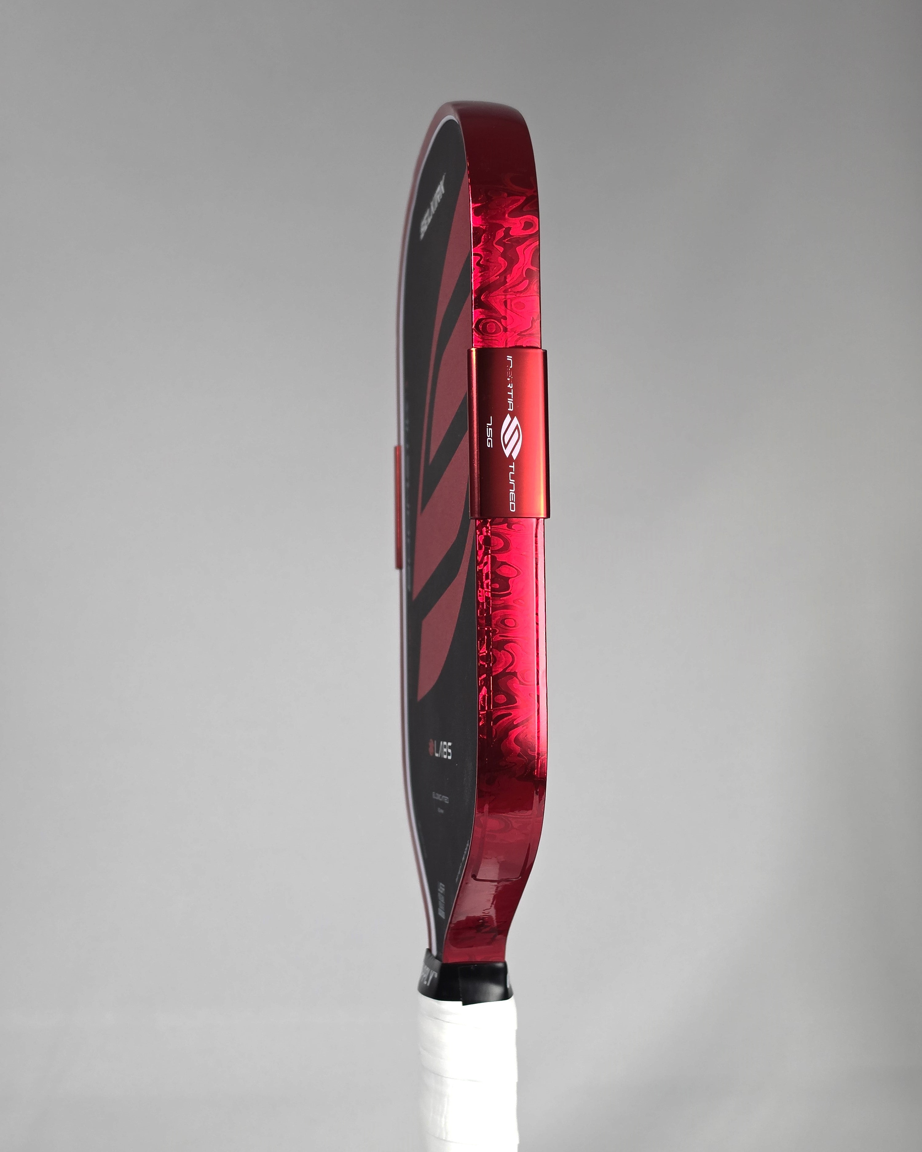 A close-up side profile of a pickleball paddle showing a Red Damascus edge tape against a gray background.