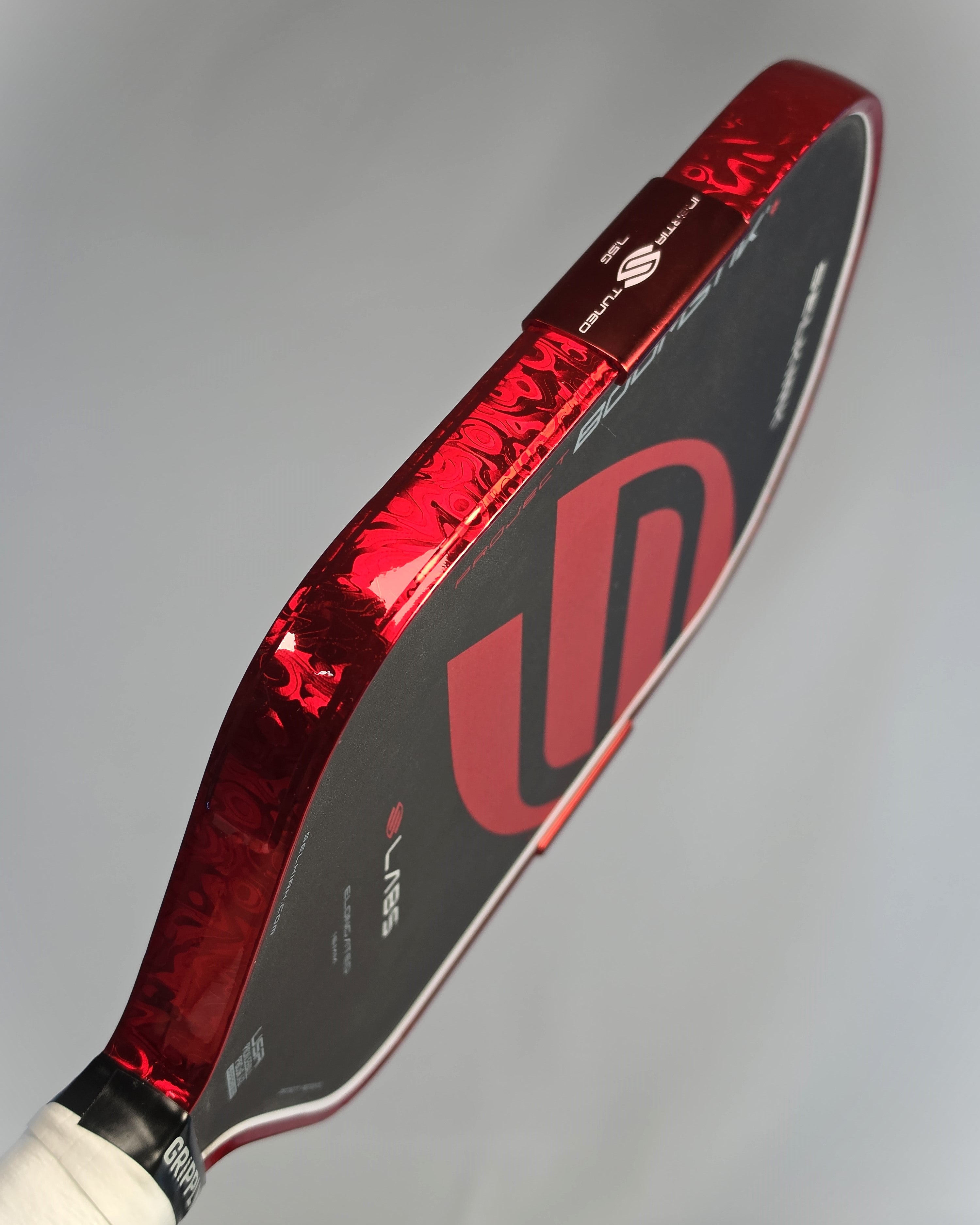 Close-up of a Boomstik pickleball paddle head showing Red Damascus Banzai Pickleball edge tape, photographed against a neutral gray background.