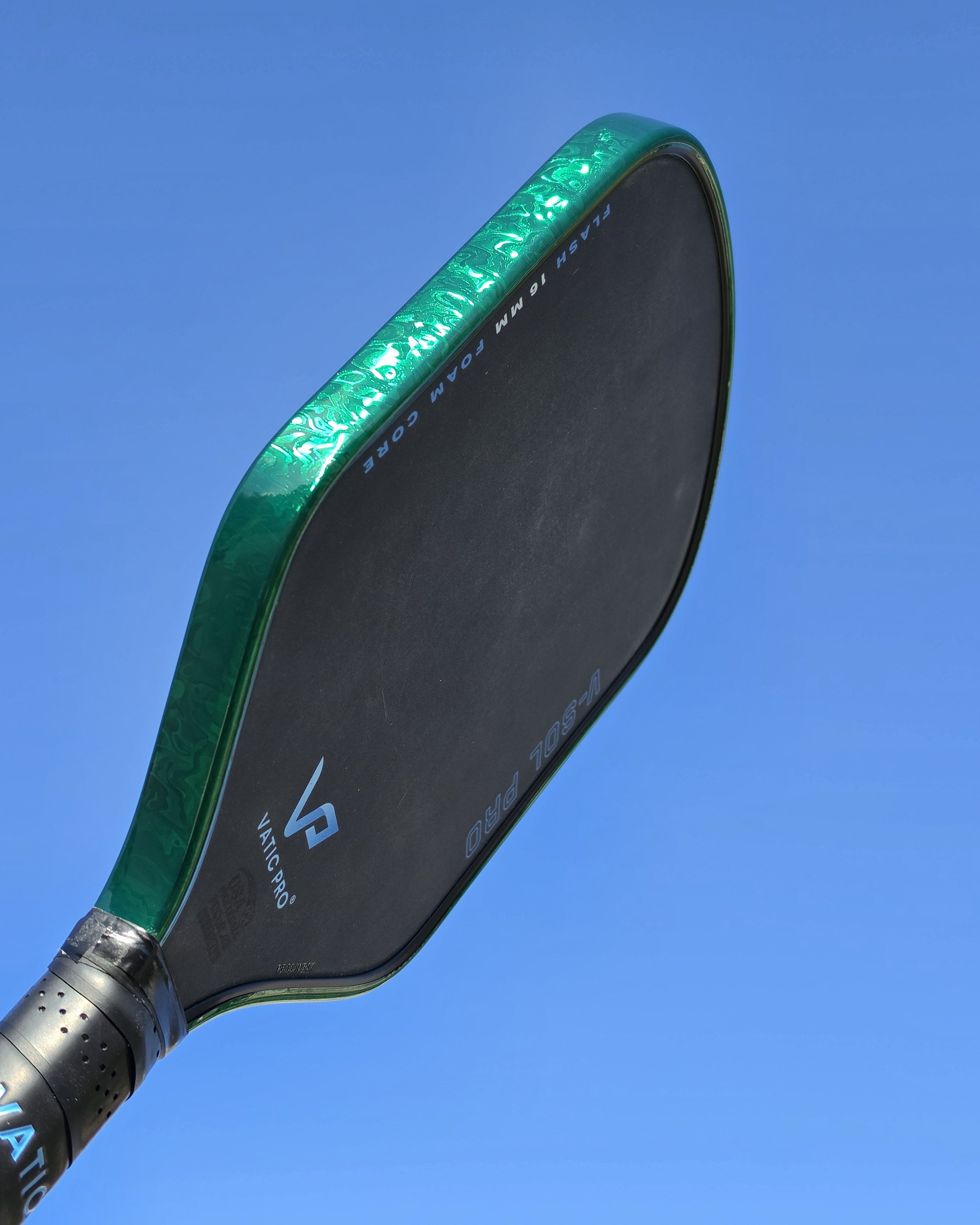 A outdoor photo of a pickleball paddle with Green Damascus edge tape against a sky background