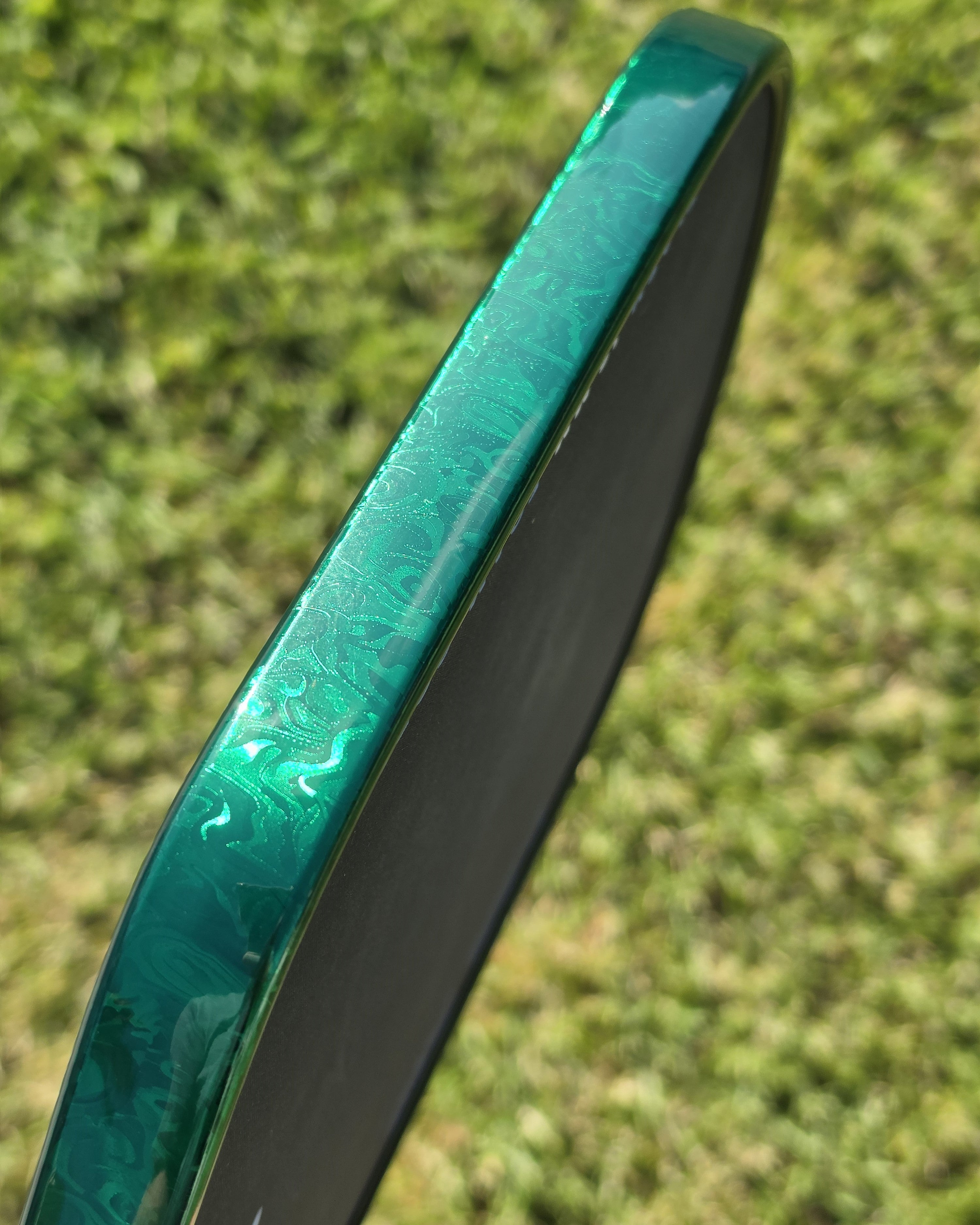 A close-up of a pickleball paddle with Green Damascus edge tape installed