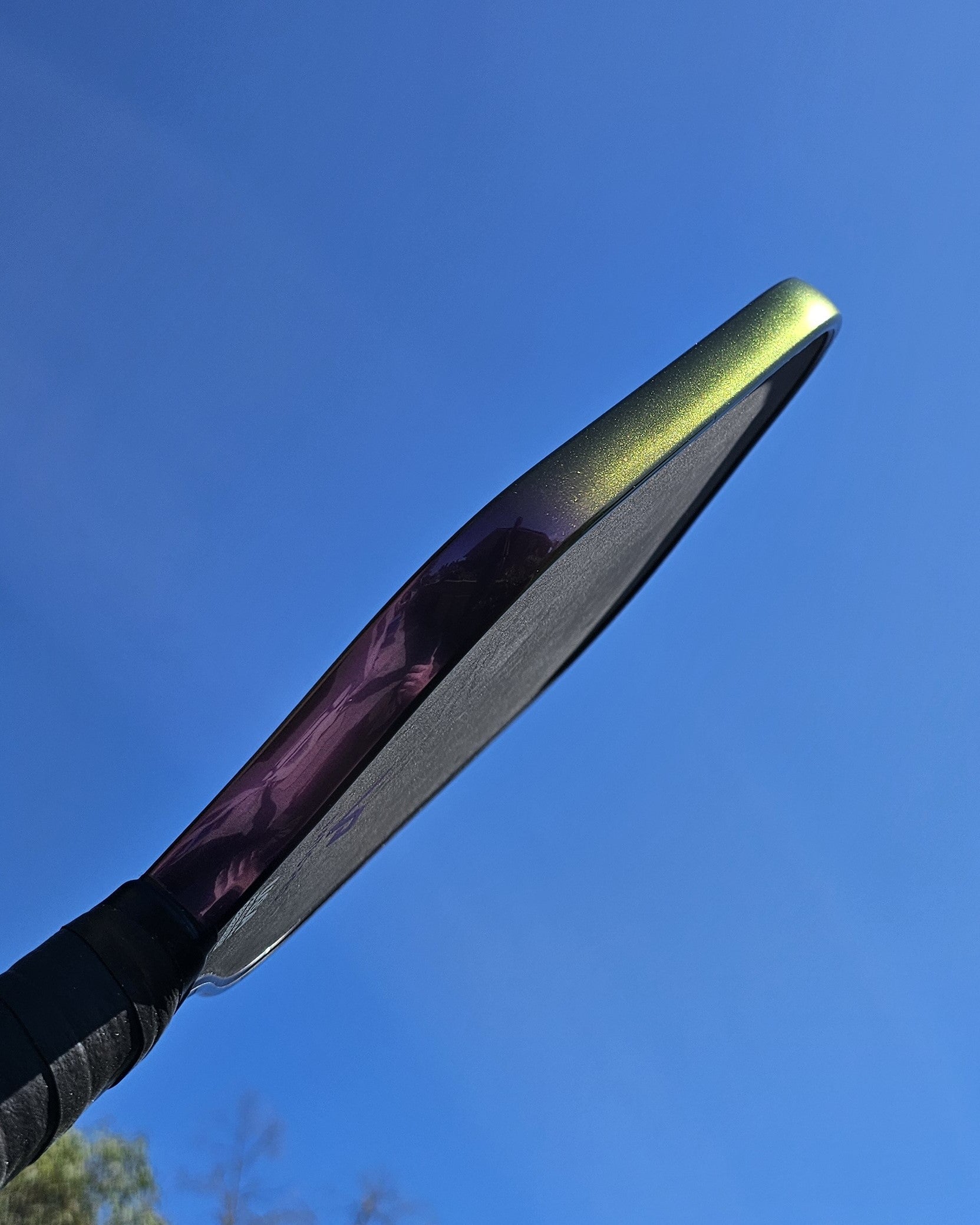 Close-up of a pickleball paddle with indigo sunset color shift edge tape.